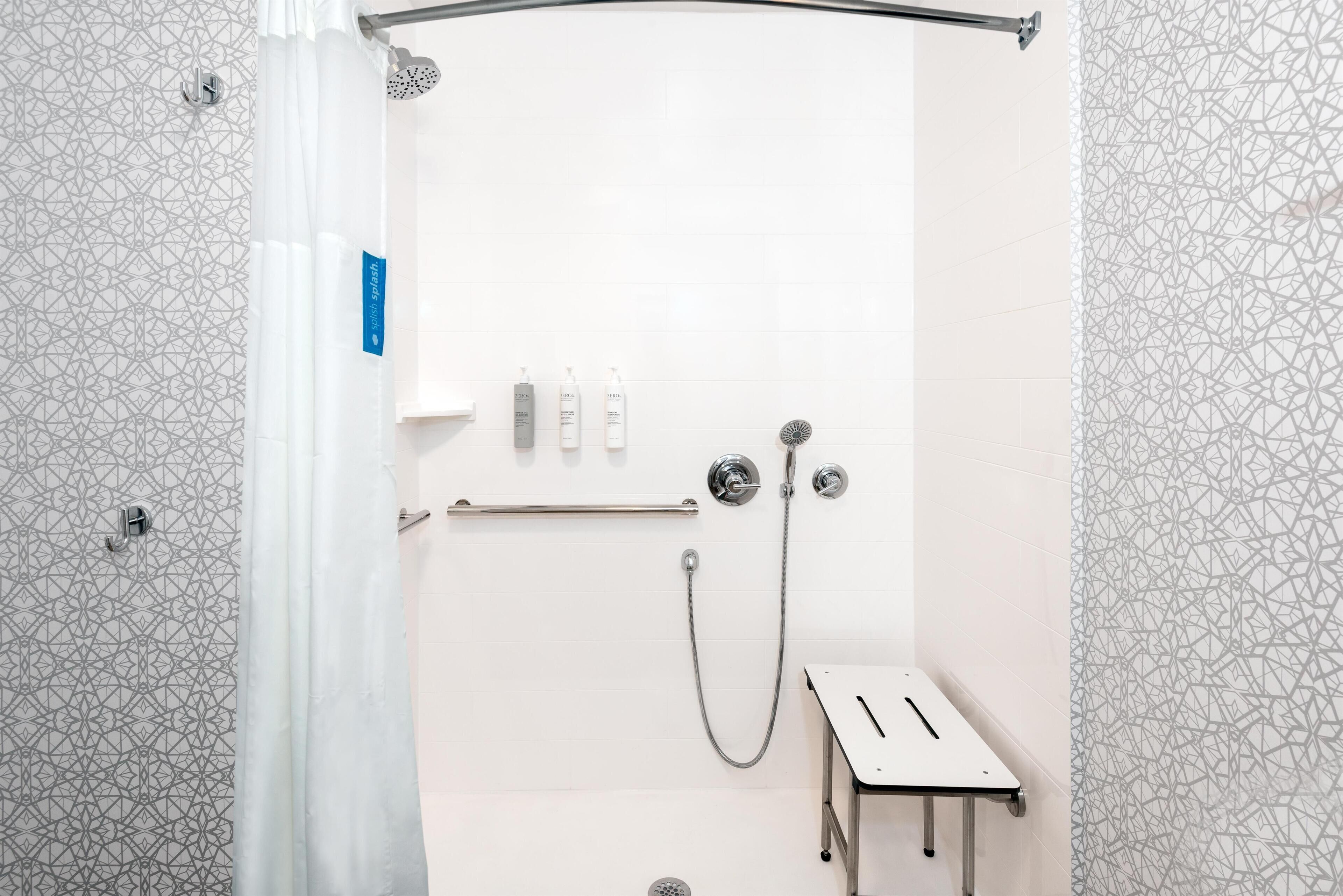 A shower area with a white tiled wall, a showerhead, a handheld shower, and a small table with a towel.