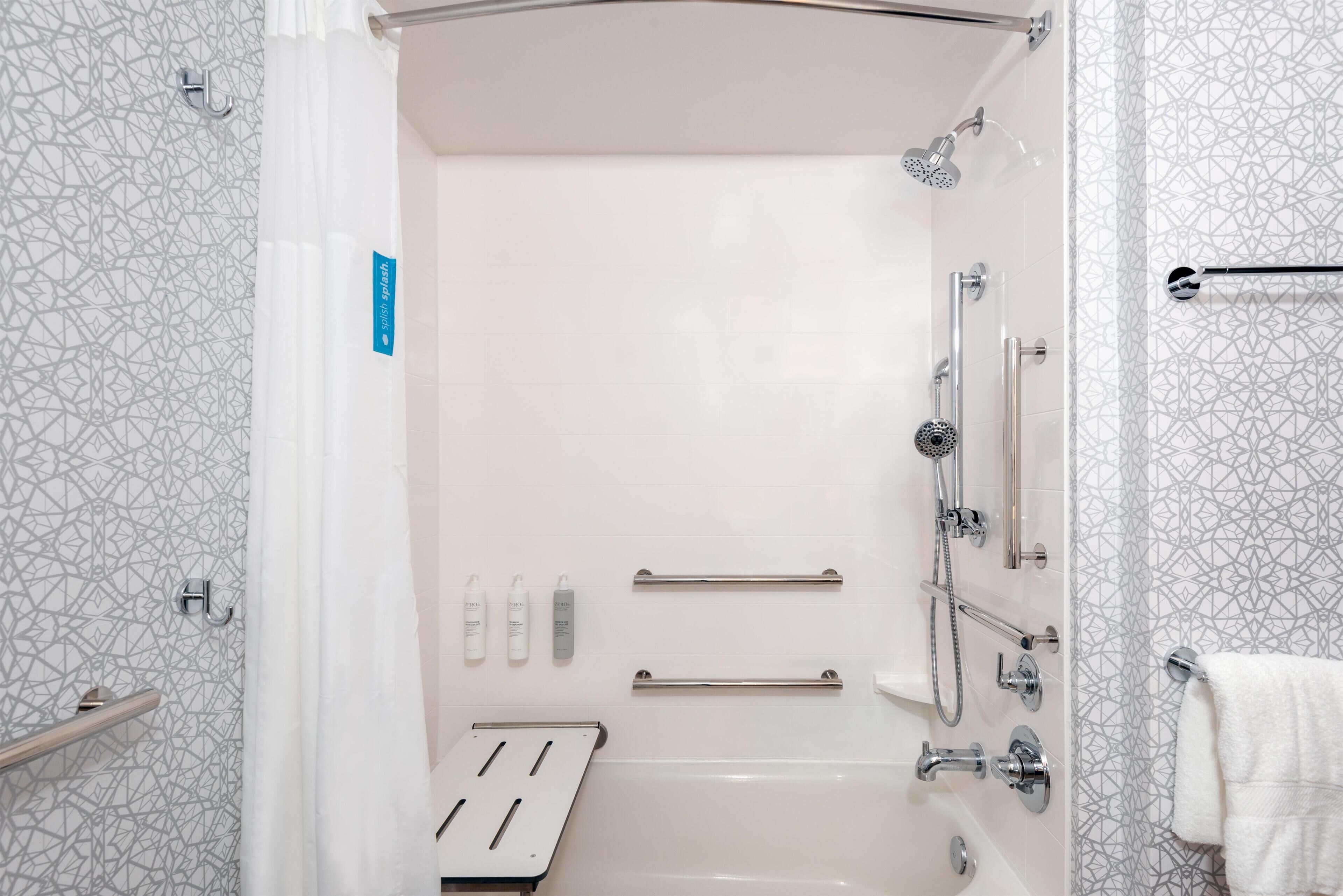 A modern bathroom with a shower, grab bars, and a towel rack.