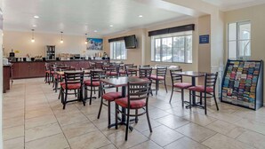 Un restaurant doté de plusieurs tables et chaises, d’un espace cuisine et d’un tableau affichant le menu.