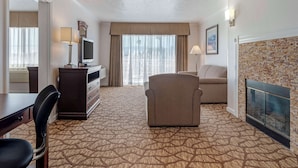 Une chambre d’hôtel avec un tapis à motifs, un canapé, un téléviseur posé sur un meuble, un bureau avec une chaise, une commode et une cheminée.