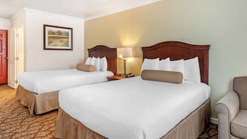 Una habitación de hotel con dos camas, una mesita de noche, una lámpara y una silla.