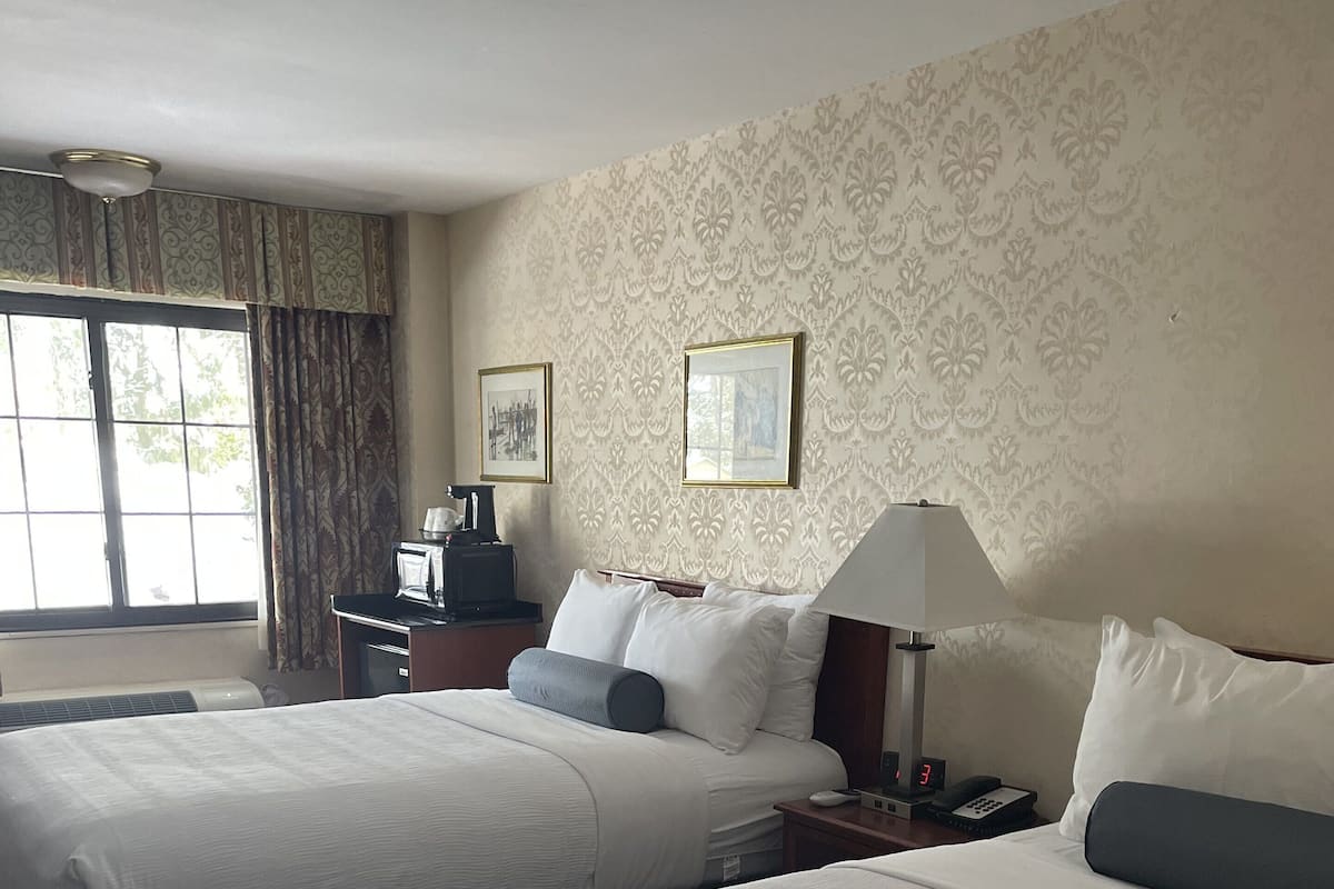 Habitación de hotel con dos camas, un escritorio, una lámpara y una ventana con cortinas.