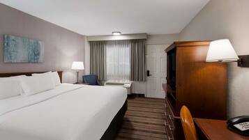 A hotel room with a large bed, a desk, a chair, a telephone, and a television.