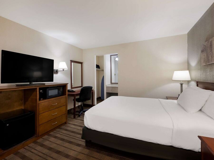 Ein Hotelzimmer mit Bett, Schreibtisch mit Fernseher, Stuhl, Schreibtischlampe und Nachttisch.