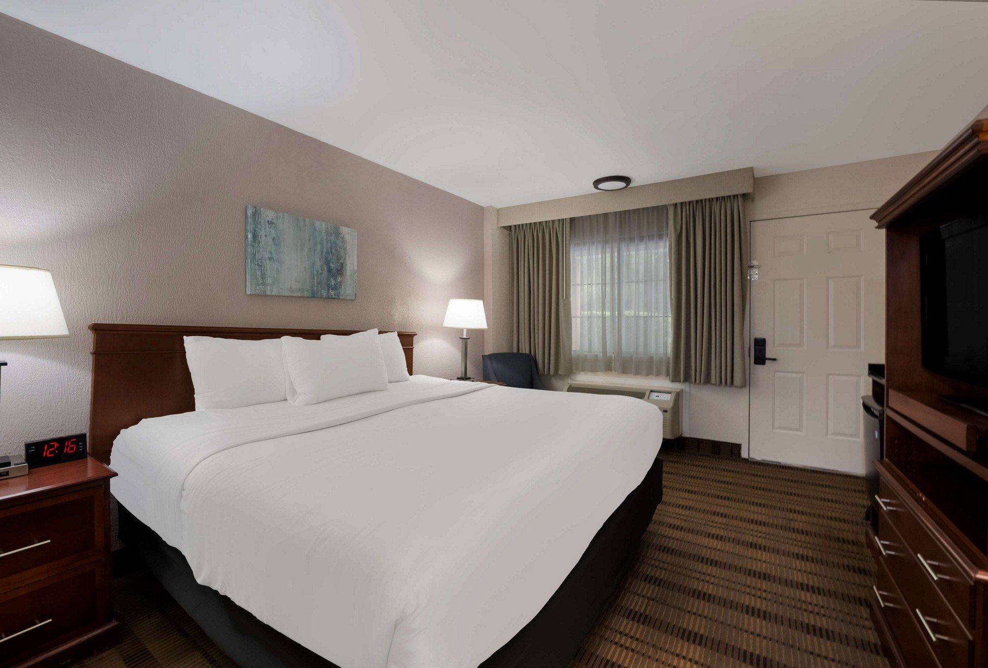 Une chambre d’hôtel avec un grand lit, des lampes de chevet, un téléviseur à écran plat, une fenêtre avec des rideaux et un tableau au mur.