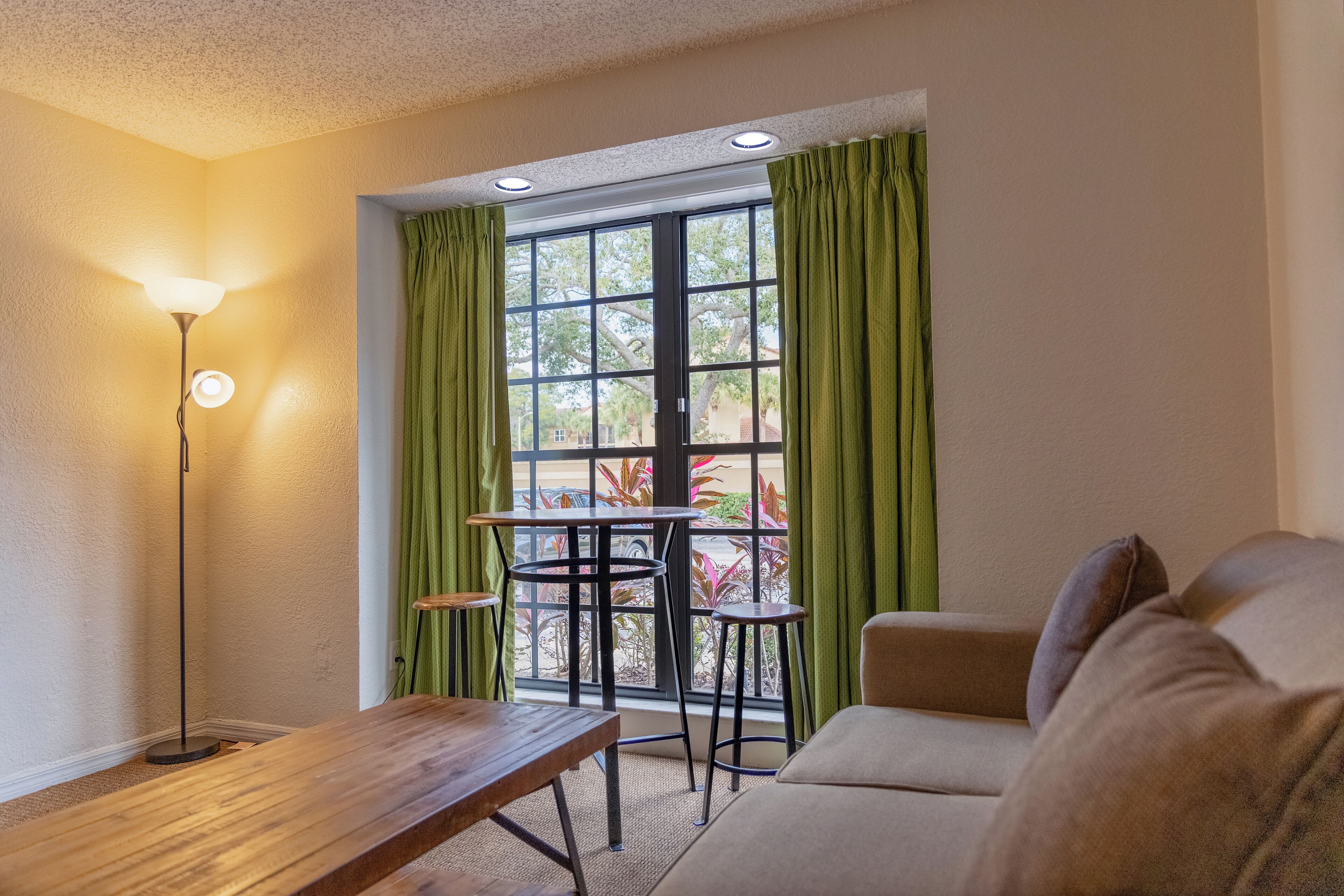 A room with a wooden table, a sofa, and a window with green curtains.