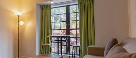 A room with a wooden table, a sofa, and a window with green curtains.