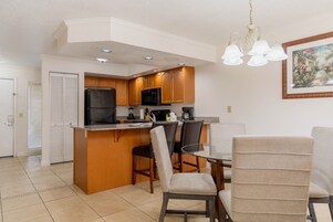 A kitchen with wooden cabinets, a black refrigerator, a microwave, and a dining area with chairs and a table.