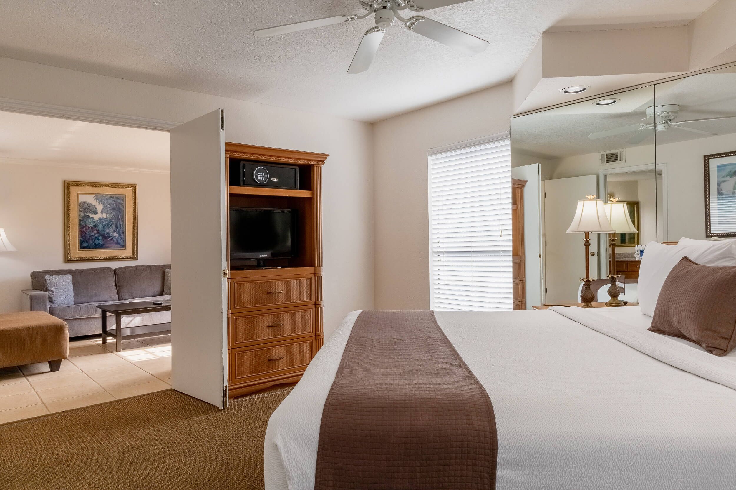 A hotel room with a bed, a television, a wooden cabinet, a sofa, and a mirror.
