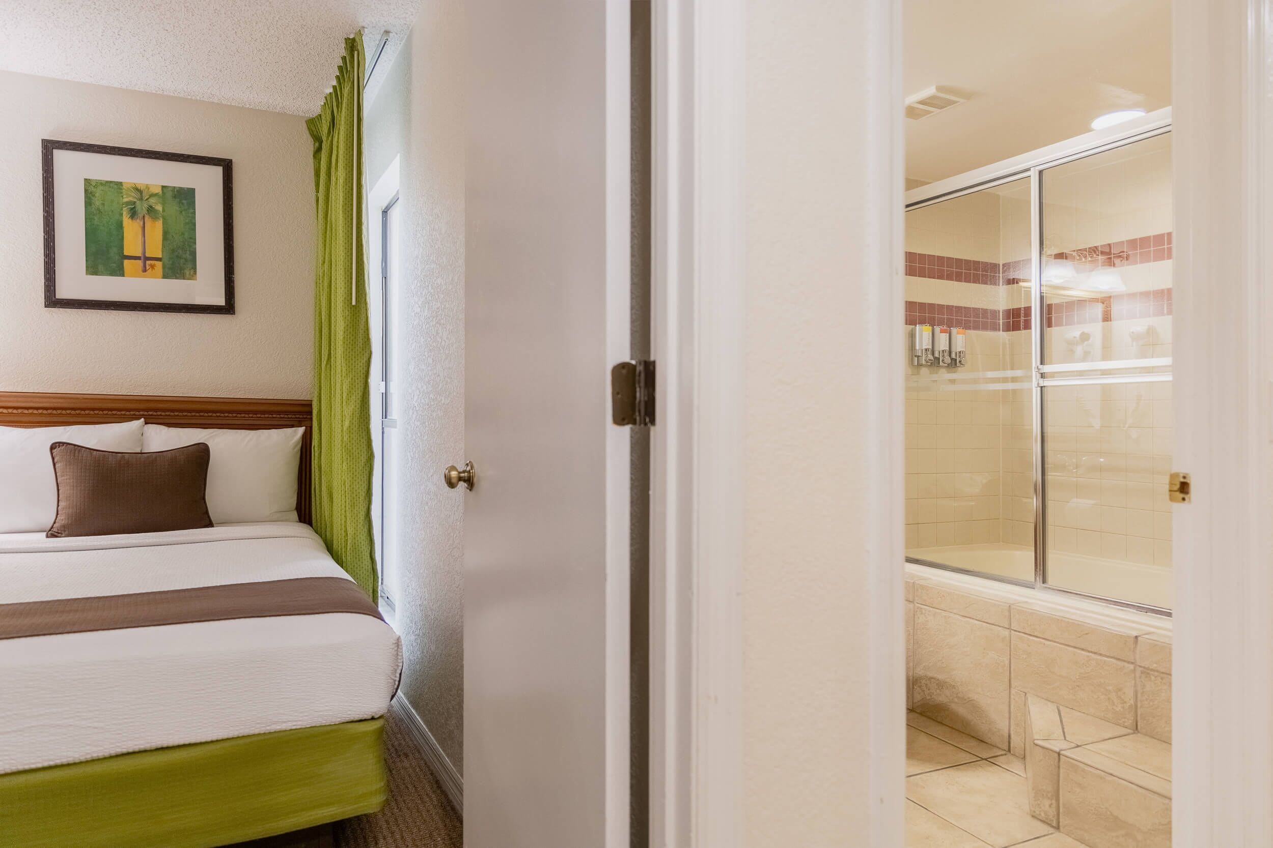 A hotel room with a bed, a framed picture on the wall, and a shower area with a glass door.