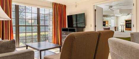 Sala de estar con un sofá, una mesa y un televisor. Hay una puerta corrediza de vidrio con cortinas.