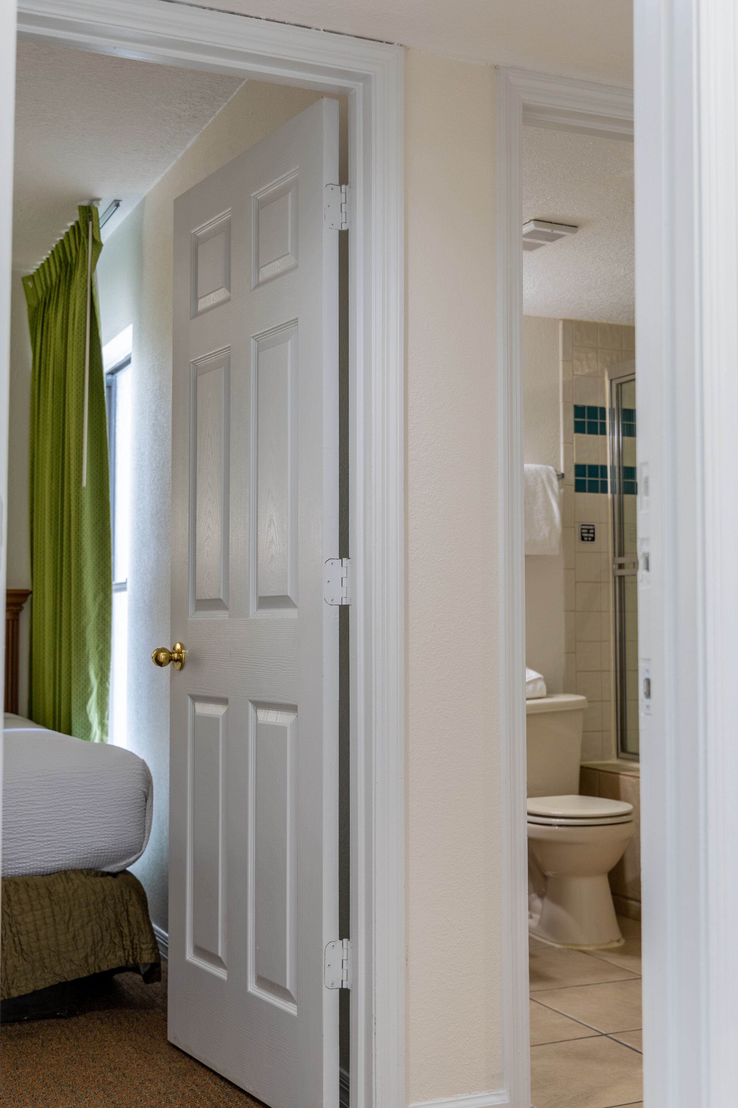 A hotel room with a bed, a bathroom with a toilet and shower, and a green curtain.