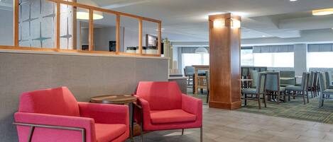 Un hall de hotel con una zona de estar que incluye sillas rojas, una mesa de madera y un pilar grande.