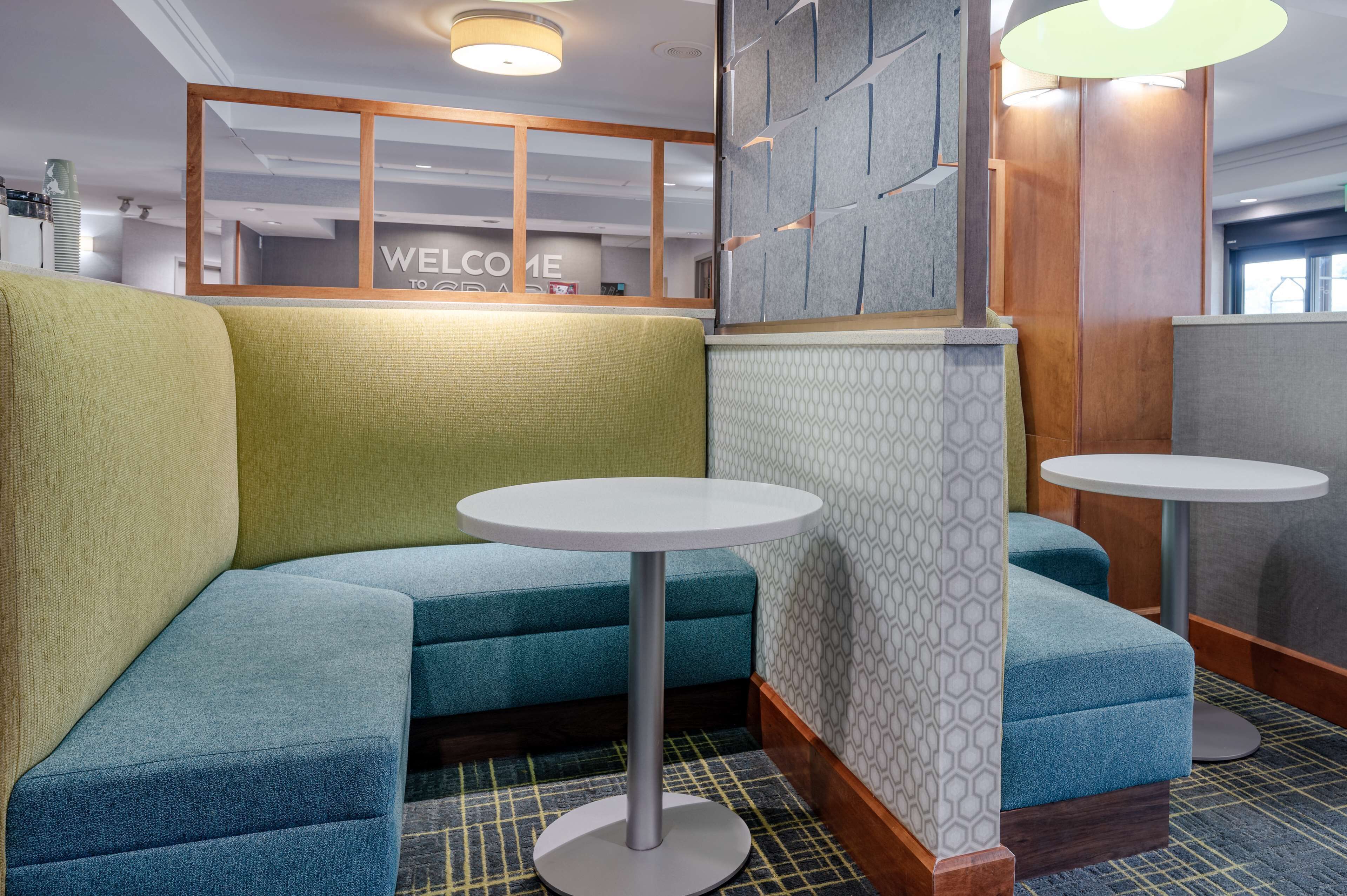 A modern waiting area with green and blue upholstered seating, a welcome sign, and a patterned wall.