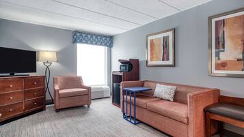 Une chambre d’hôtel équipée d’un téléviseur à écran plat, d’un canapé, d’un fauteuil, d’une petite table et d’un radiateur.