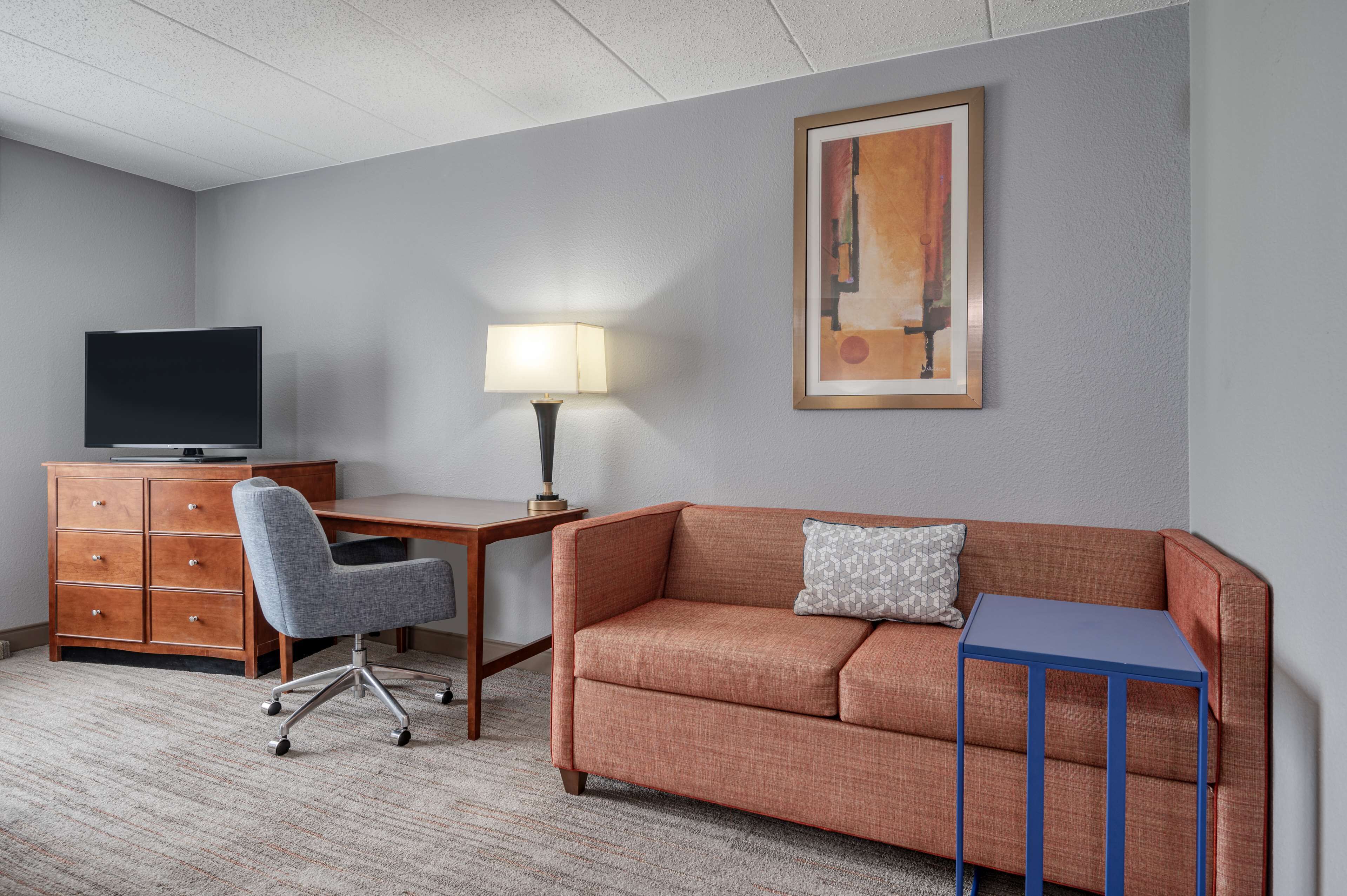 A hotel room with a sofa, a desk, a television, a lamp, and a framed picture on the wall.