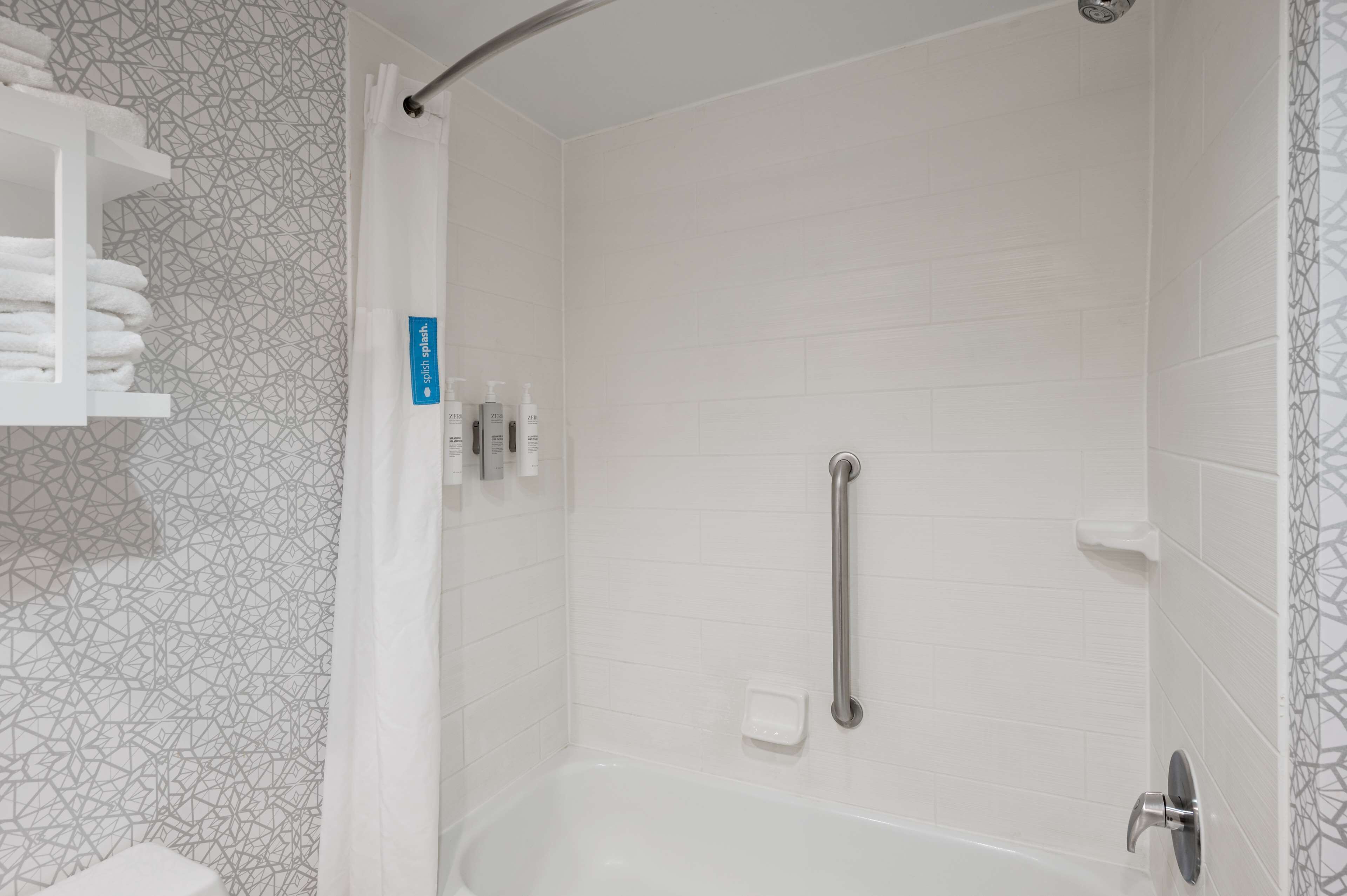 Un área de ducha con una bañera blanca, un asidero y un estante con toallas.