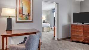 Una habitación de hotel con escritorio, silla, televisión y un cuadro en la pared.