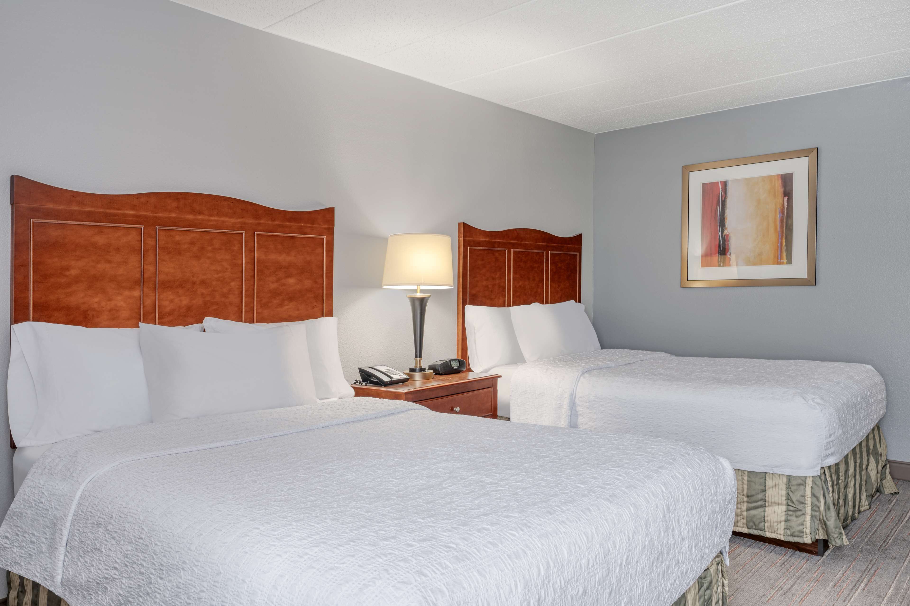 A hotel room with two beds, a nightstand with a lamp, and a framed picture on the wall.