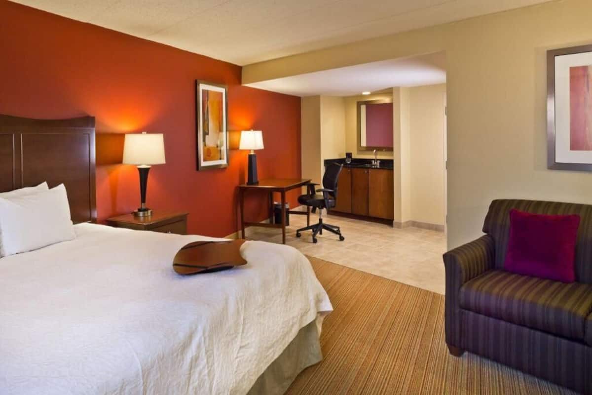 A hotel room with a bed, two bedside lamps, a desk with a chair, a small table, and a sofa.
