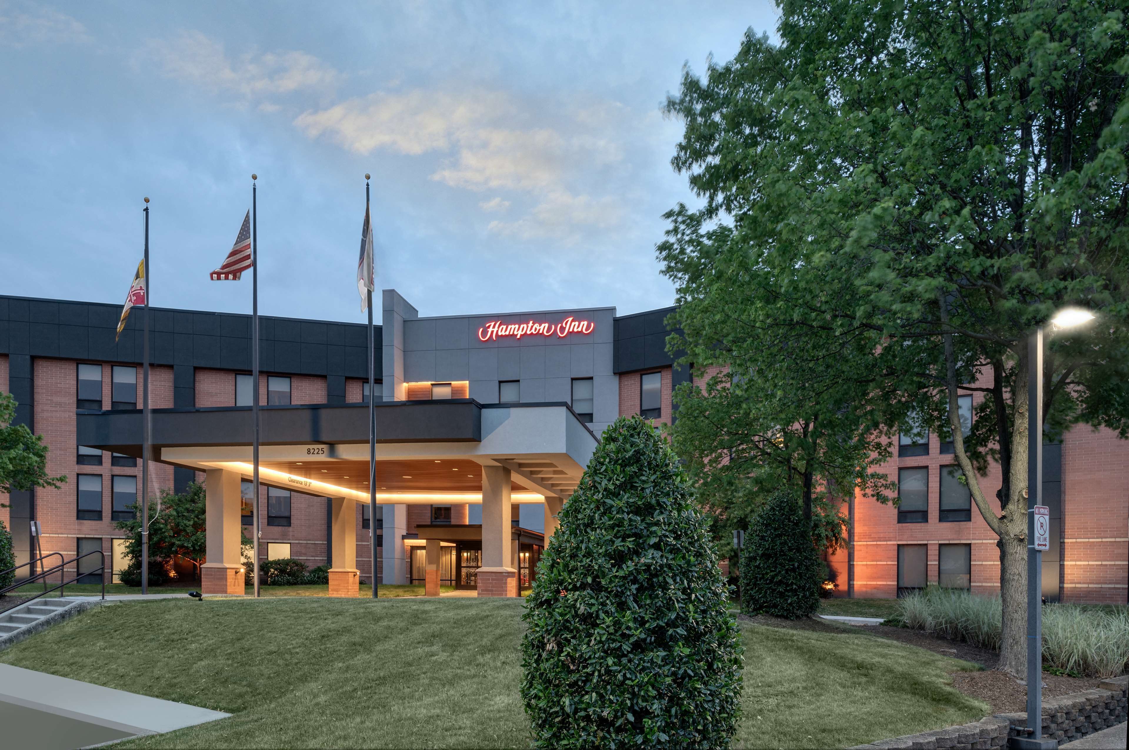 A Hampton Inn hotel with a modern design, featuring a covered entrance and multiple flags.