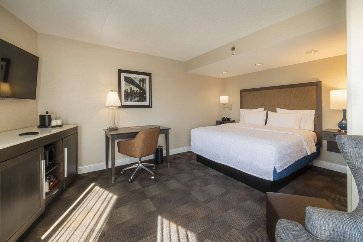 Une chambre d’hôtel avec un lit, un bureau, une chaise et un téléviseur fixé au mur.