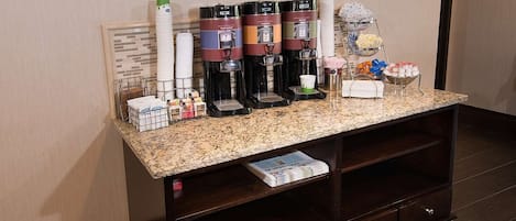 A hotel reception area with a coffee station, a newspaper rack, and framed artwork on the wall.