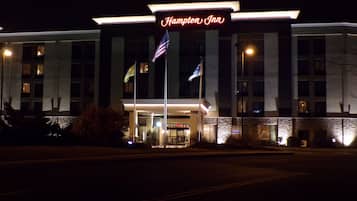 A Hampton Inn hotel with a prominent illuminated sign, multiple flags, and a well-lit entrance.