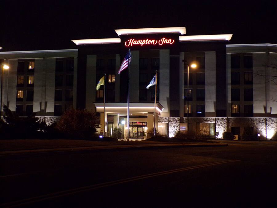 A Hampton Inn hotel with a prominent illuminated sign, multiple flags, and a well-lit entrance.