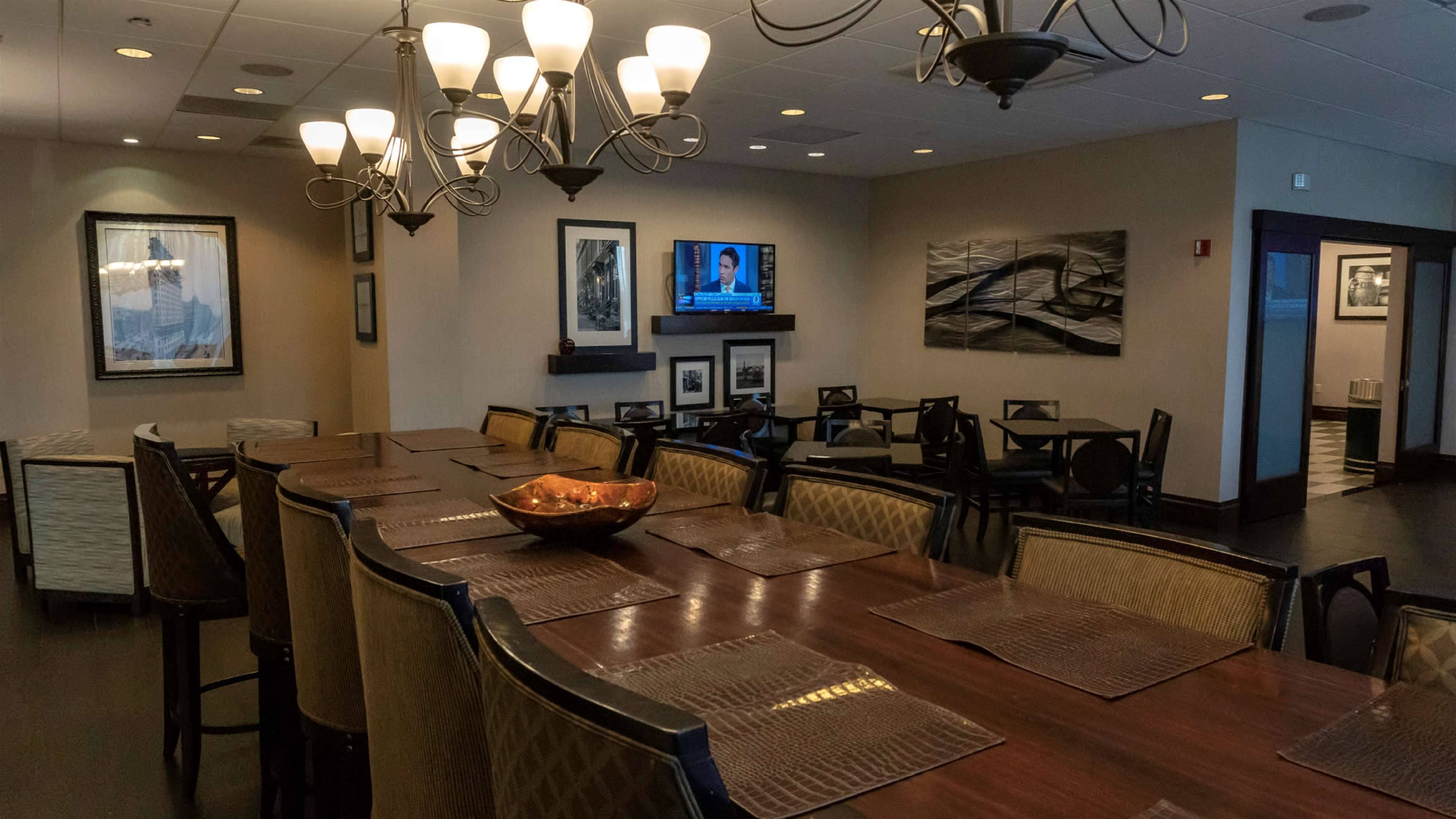 A conference room with a large oval table, multiple chairs, a bowl of fruit, a television, framed pictures, and a chandelier.