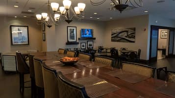 A conference room with a large oval table, multiple chairs, a bowl of fruit, a television, framed pictures, and a chandelier.