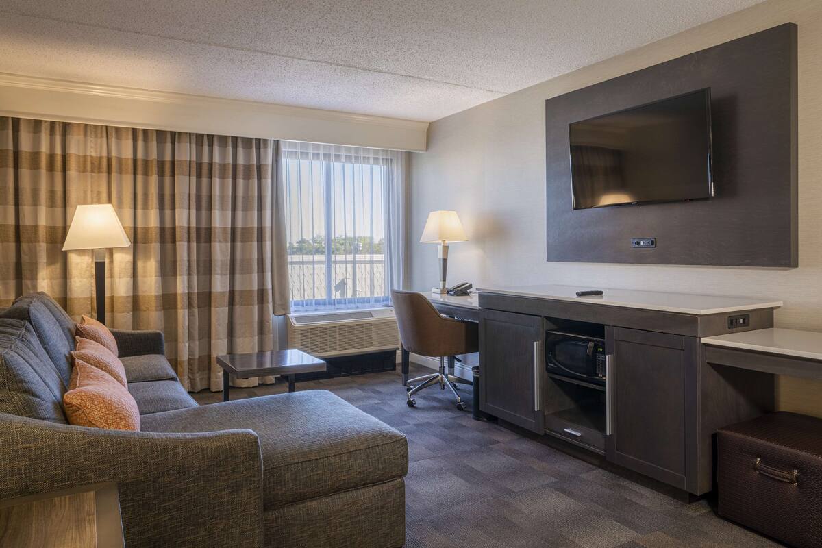 Une chambre d’hôtel équipée d’un canapé, d’un bureau, d’une télévision à écran plat, d’une lampe, d’une chaise et d’un four à micro-ondes.