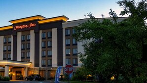 Un hotel Hampton Inn con diseño moderno, destacando una entrada principal y una señal de parada al frente.