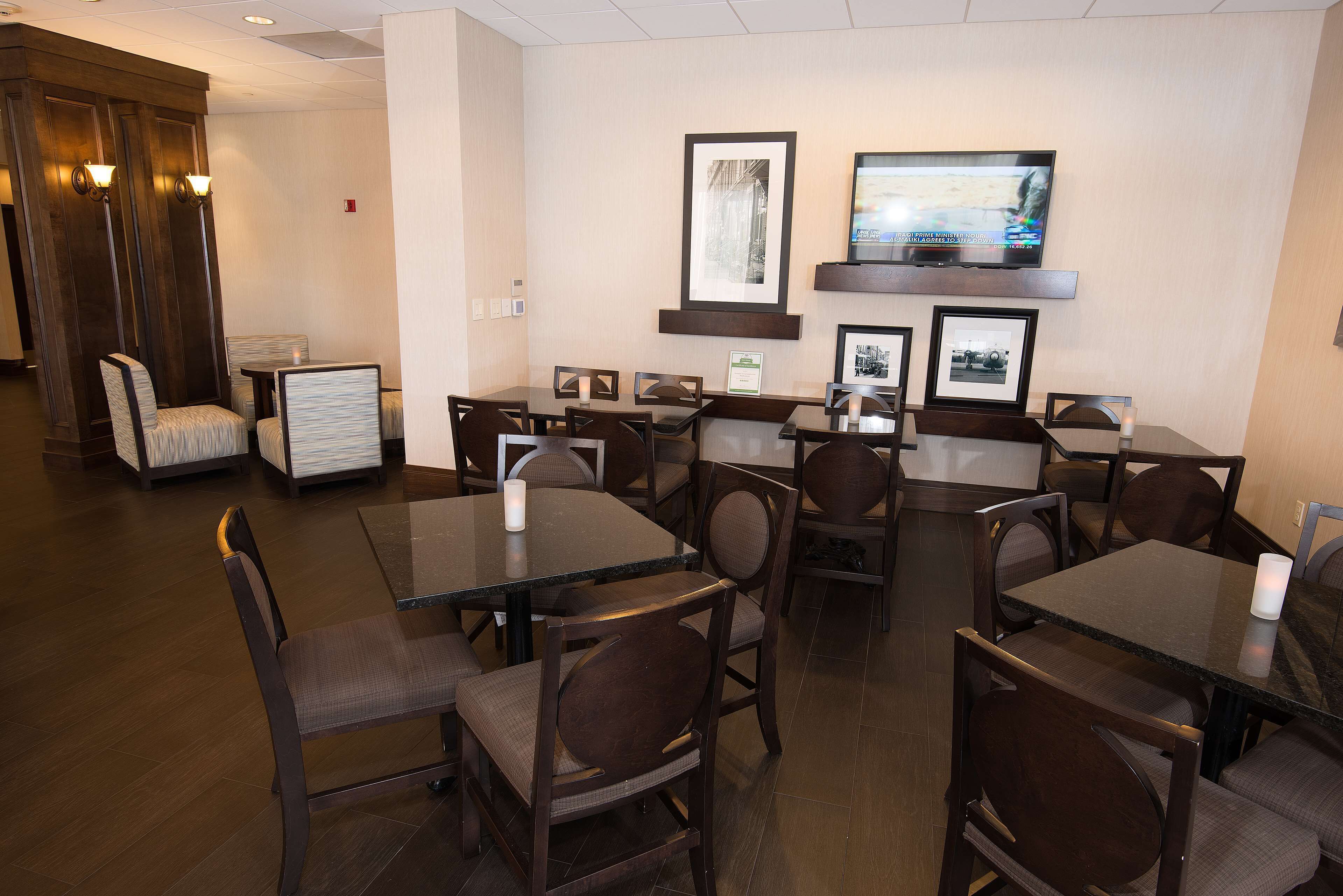 Un comedor de hotel con varias mesas y sillas, cuadros en las paredes y un televisor sobre las mesas.