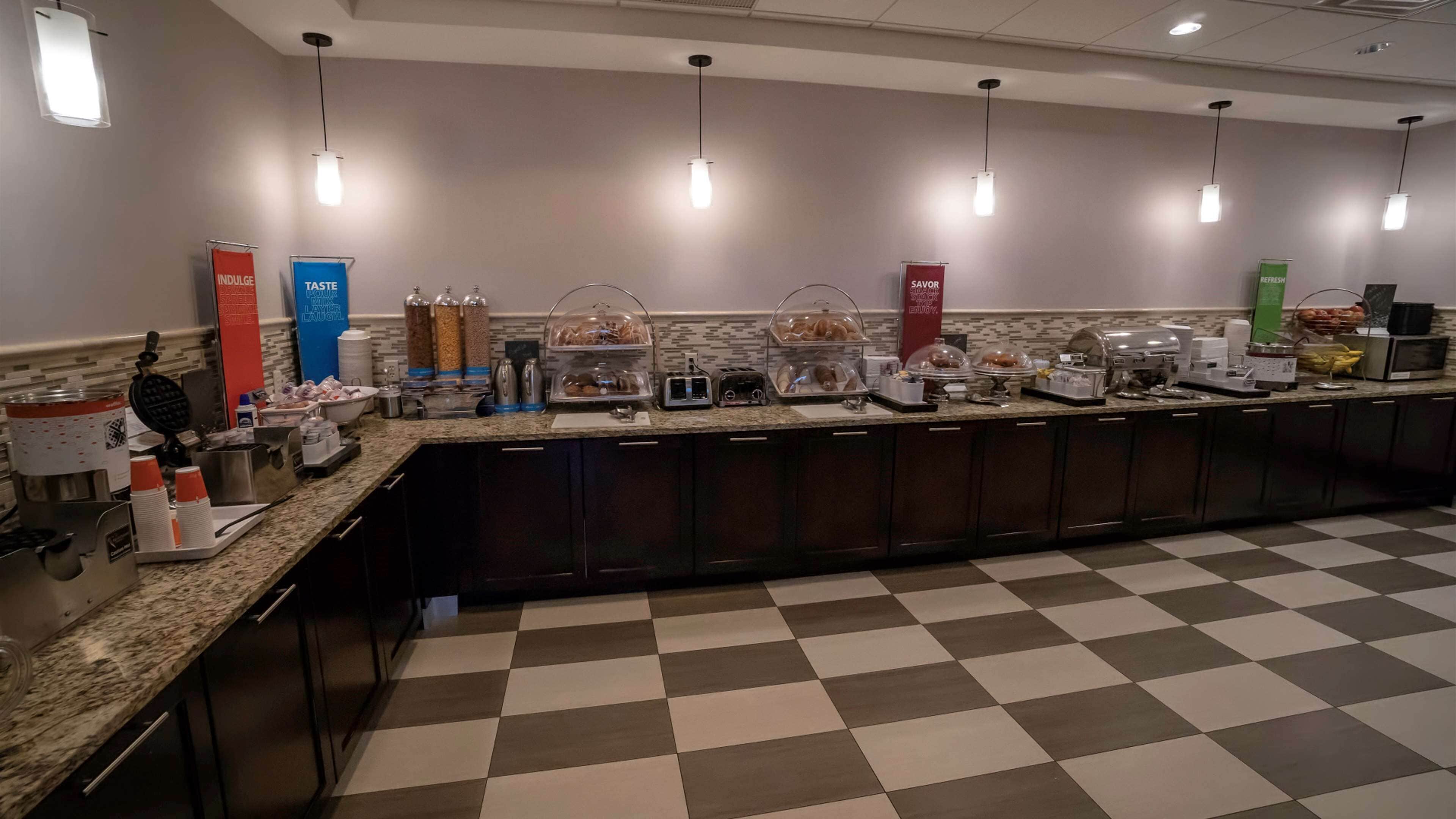Un área de bufé con distintas estaciones de comida, incluyendo una de café, una de bebidas y una barra de ensaladas.