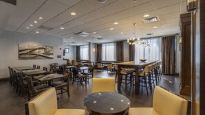 Un amplio comedor de hotel con múltiples mesas y sillas, ventanas grandes con cortinas y un candelabro.
