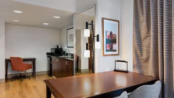 Une chambre d’hôtel équipée d’une table à manger, d’une chaise, d’un canapé, d’un coin cuisine et d’une grande fenêtre avec des rideaux.