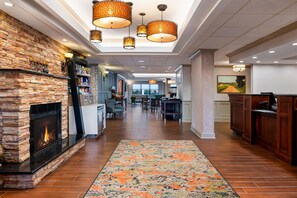 A hotel lobby with a fireplace, a dining area, and a bar. - Hampton Inn South Hill (South Hill)
