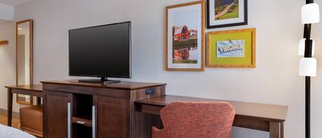 Habitación de hotel con una televisión de pantalla plana sobre un escritorio de madera, una silla tapizada en rojo y cuadros en la pared.