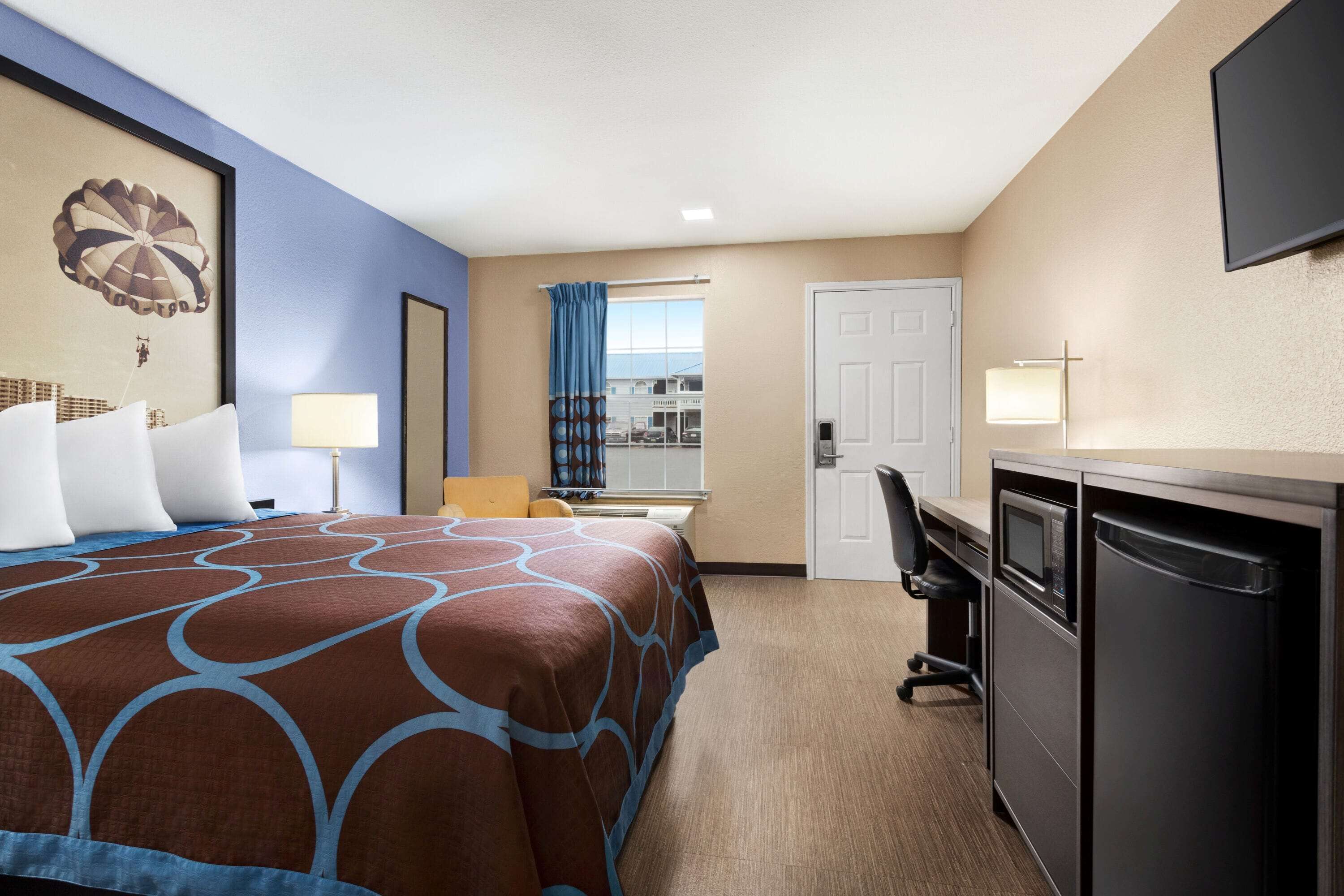 Una habitación de hotel con una cama grande, un escritorio, una silla, un televisor y una puerta.