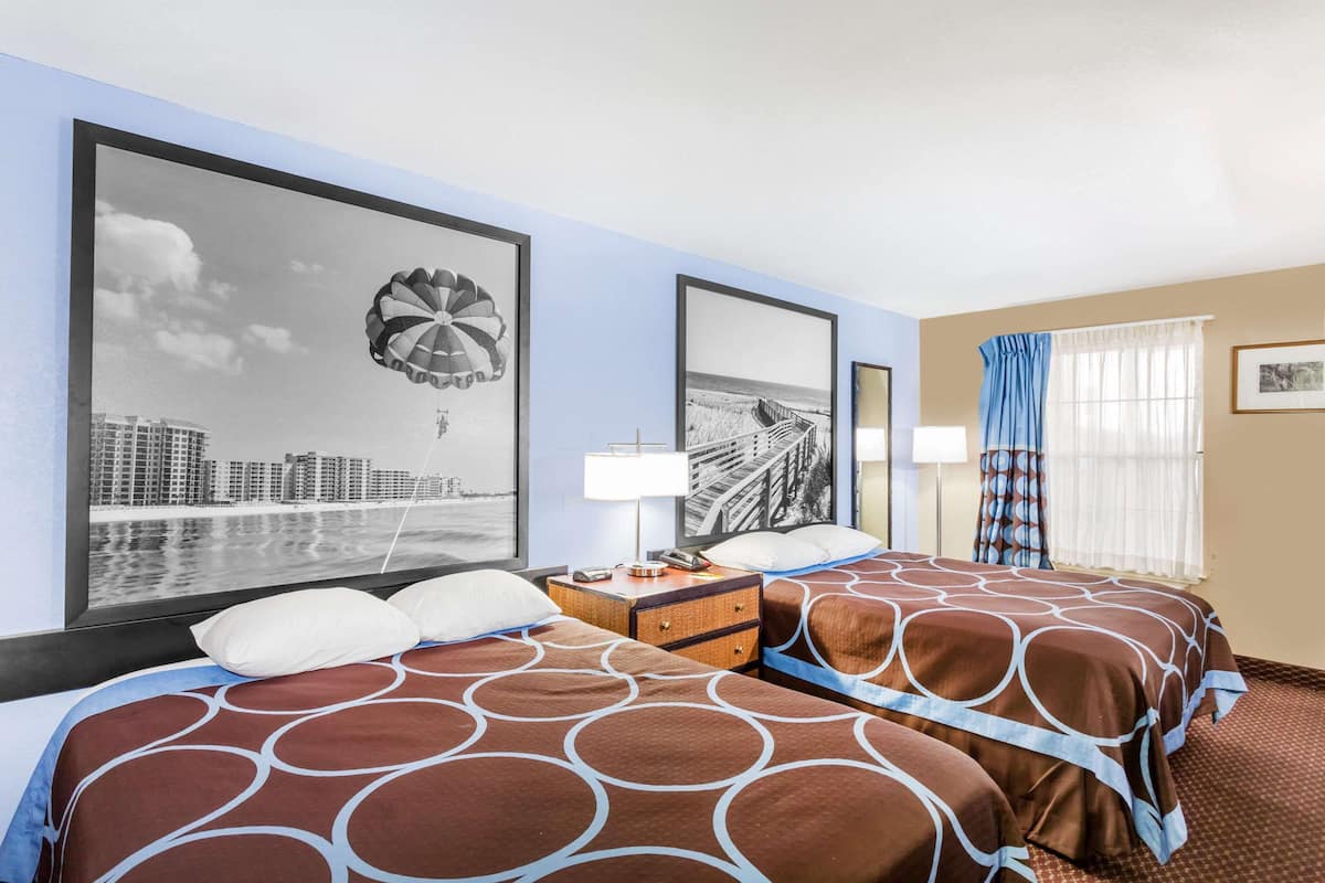 A hotel room with two beds, a cityscape view, a large window with curtains, and a nightstand with a lamp.