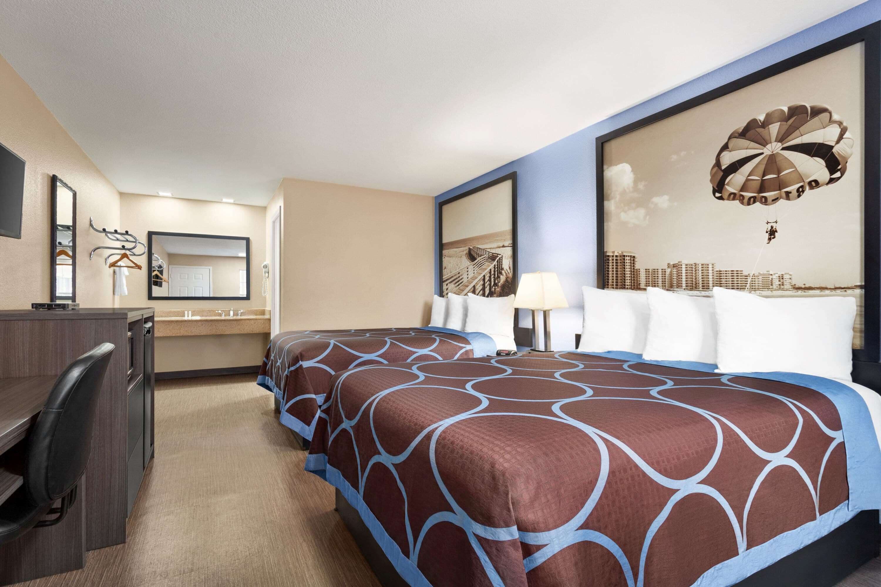 A hotel room with two beds, a desk, a chair, a mirror, and a large framed picture on the wall.