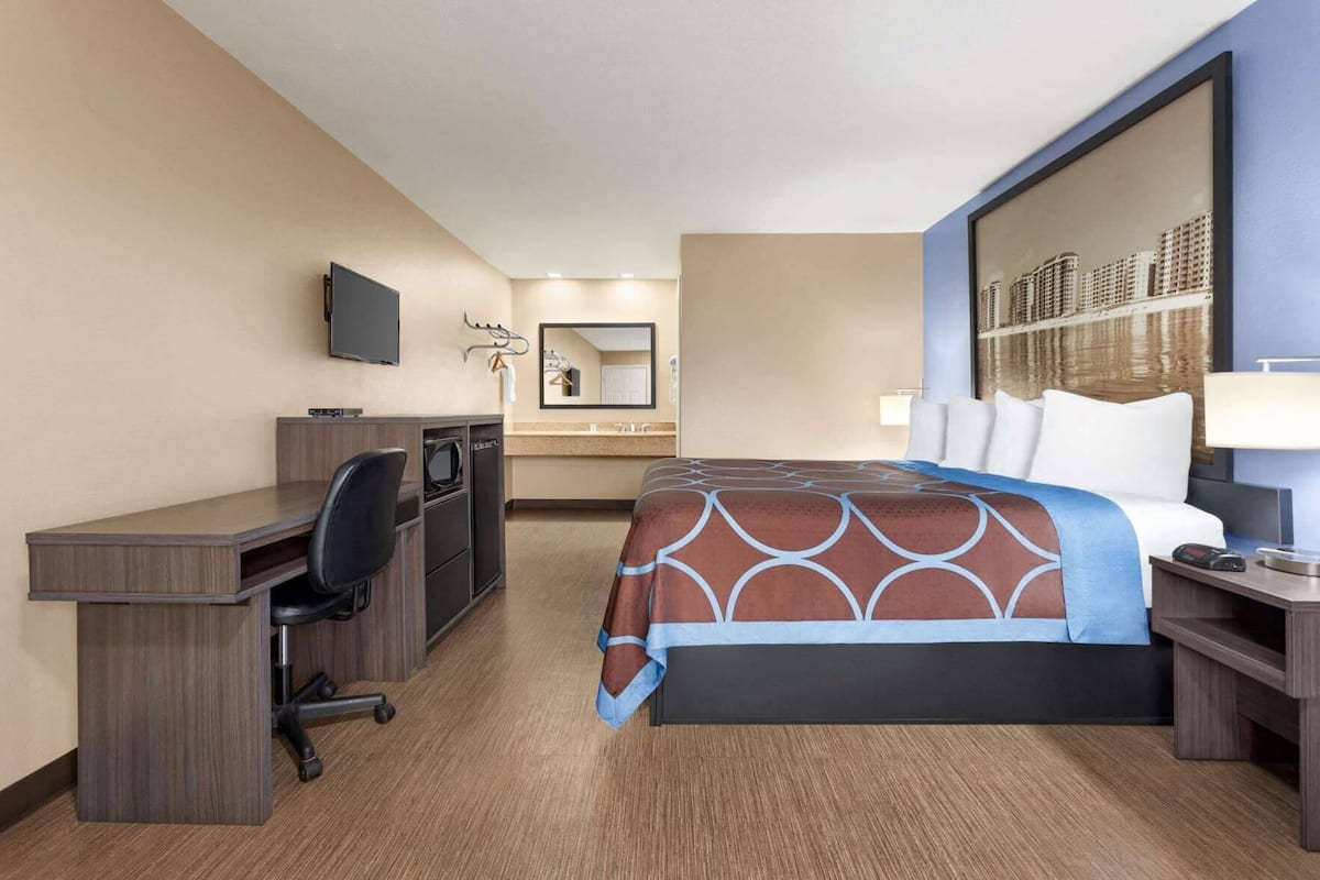 A hotel room with a bed, desk, chair, and a television.