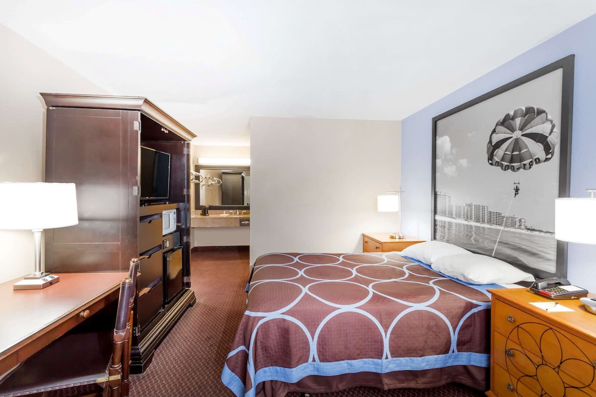 A hotel room with a bed, a desk, a dresser, a TV, a mirror, and a cityscape artwork on the wall.