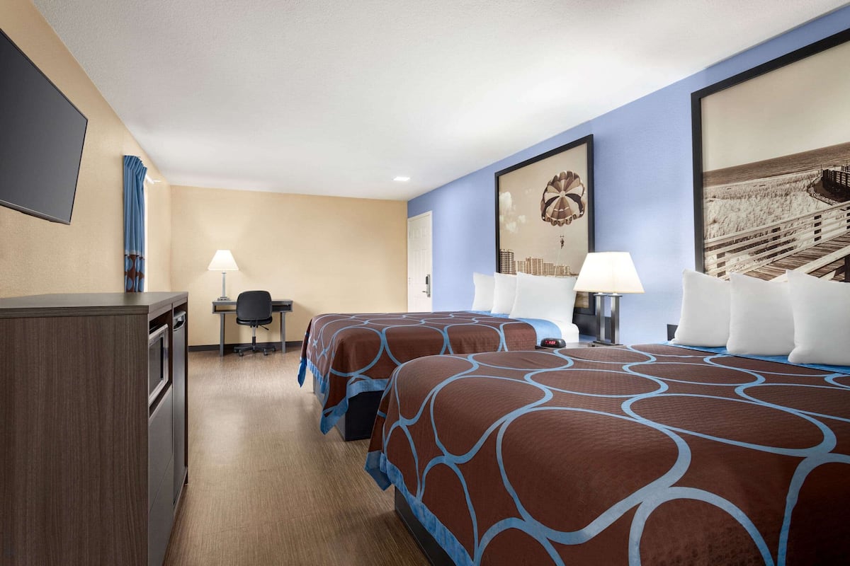 A hotel room with two beds, a desk, a chair, a TV, and a large window.