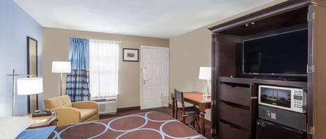 A hotel room with a bed, a desk, a chair, a television, a microwave, and a door.