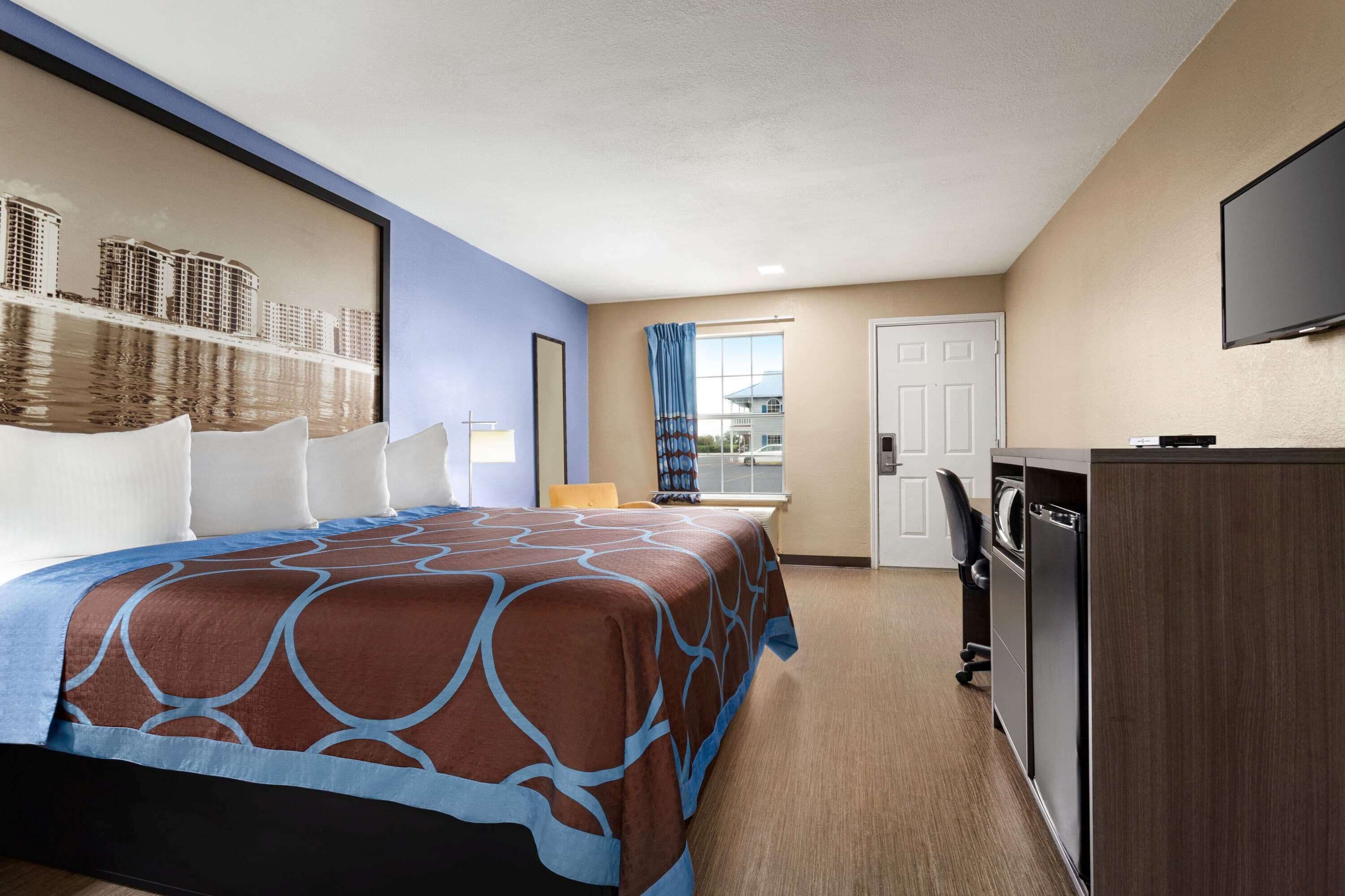 Une chambre d’hôtel avec un grand lit, un bureau, une chaise, une télévision et une fenêtre avec des rideaux.