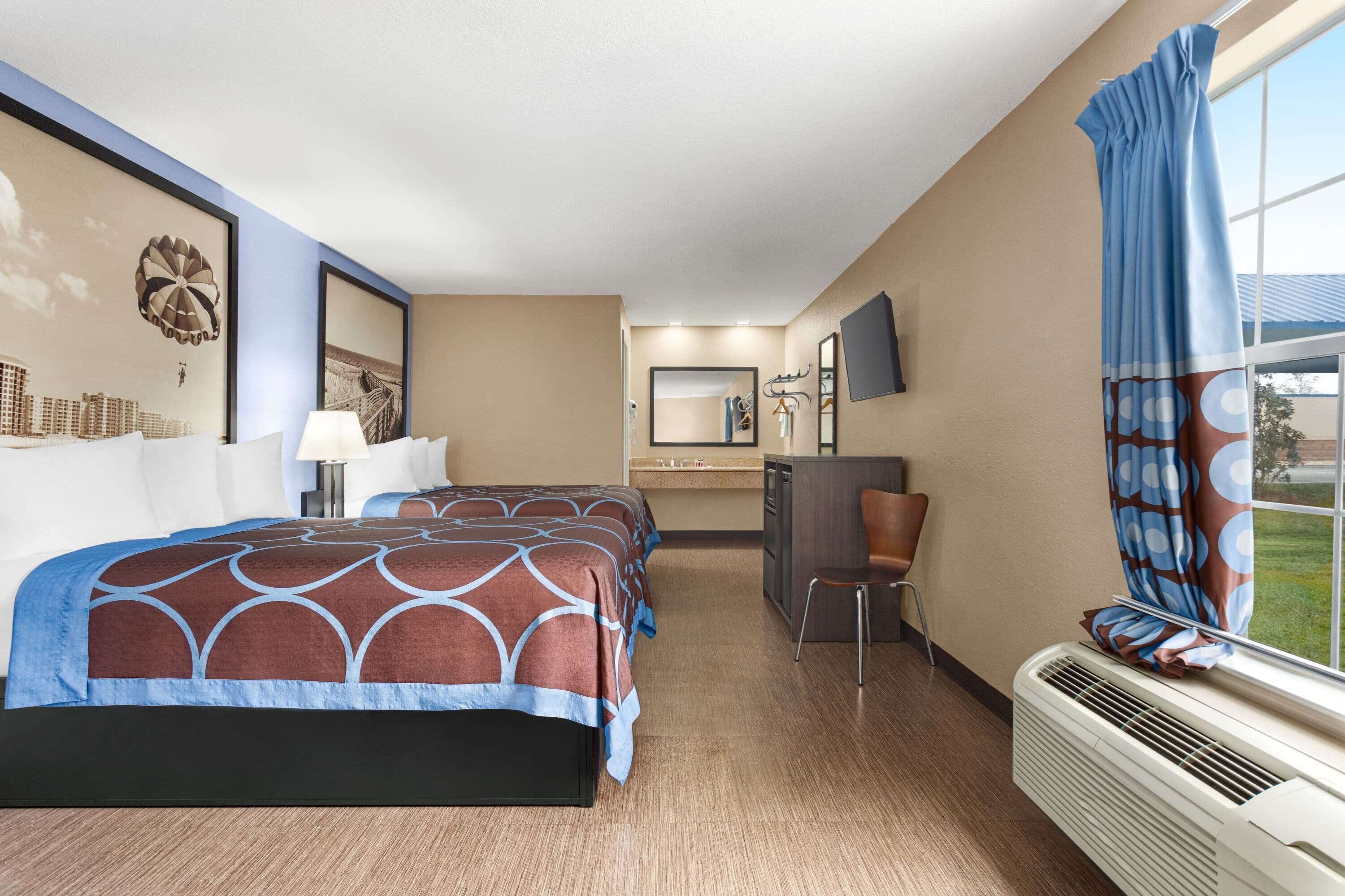 A hotel room with two beds, a desk, a chair, a TV, and a window with curtains.