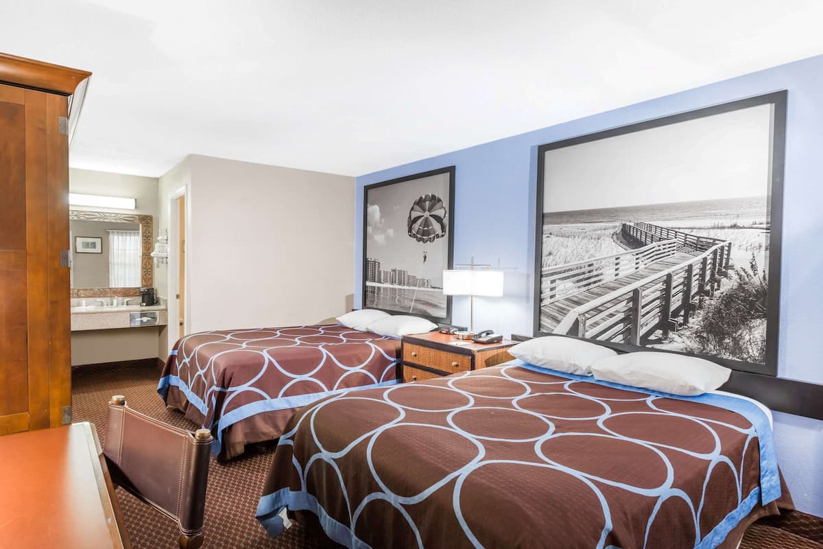 A hotel room with two beds, a desk, a dresser, and a large window with a beach view.