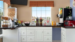 A kitchen with white cabinets, a coffee machine, a microwave, and a window with a view of the outside.